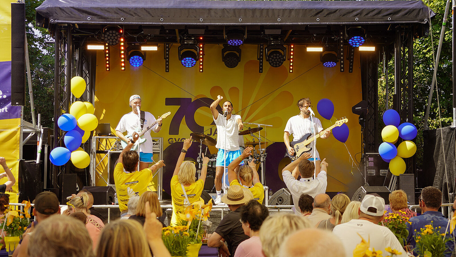 Eine Band spielt auf einem Fest auf einer Bühne bei sommerlichem Wette vor Publikum