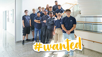 Foto der aktuellen Azubis der GVG Rhein-Erft, die als Gruppe am Treppenaufgang zusammenstehen. Auf dem Bild steht das Wort "Wanted".