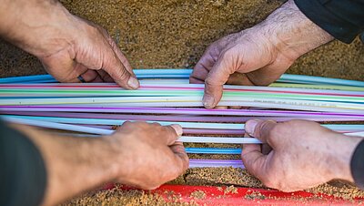 Mehrere helfende Hände bauen bunte Glasfaser in den Boden