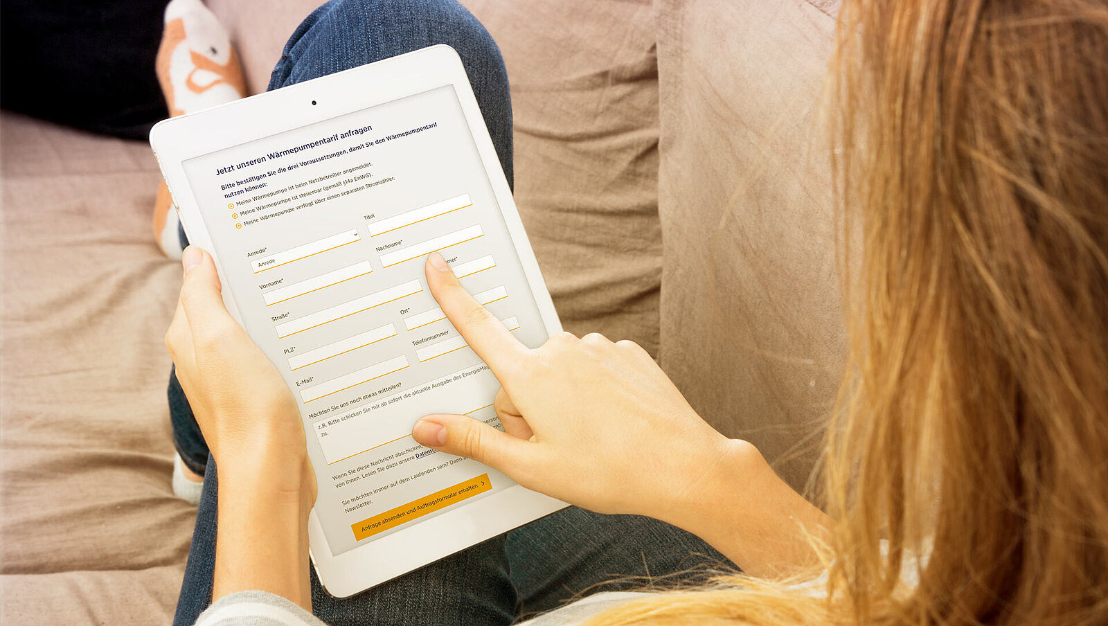Frau auf einer Couch mit einem Tablet in der Hand. Geöffnet ist die Website der GVG und die Frau tippt auf ein Formularfeld.